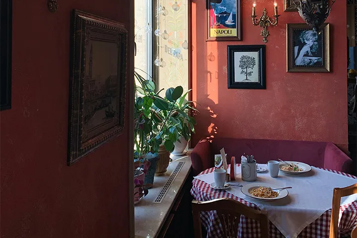 Röd trattoria-interiör med rutig duk och två tallrikar pasta